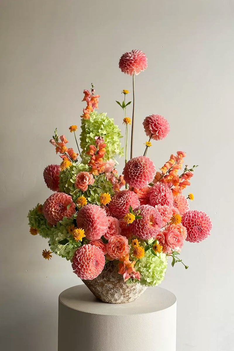 Colorful flower arrangement on a white pedestal against a plain background