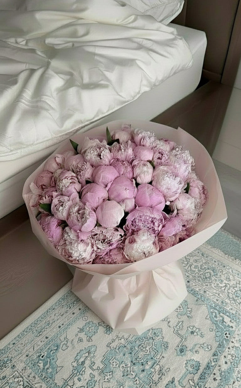 Bouquet of pink and white peonies in a white paper wrap on a Turkish rug.